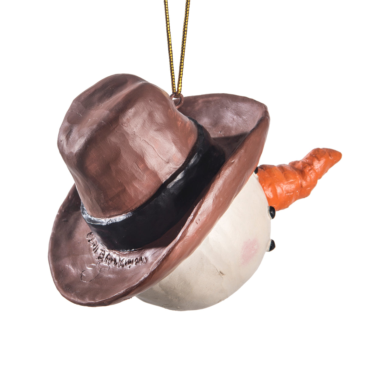 A snowman Christmas ornament wearing a brown cowboy hat with a black band and an orange carrot nose, hanging by a gold string against a white background.