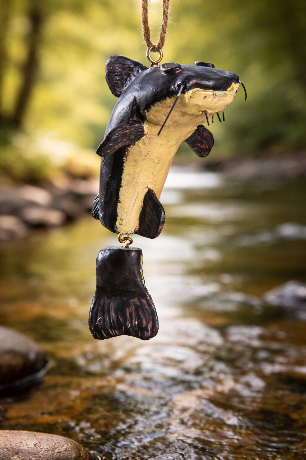 Decorative catfish ornament hanging over a stream with blurred natural background