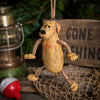 A rustic resin dog hanging ornament with rope limbs and a hanging loop, styled on a wooden surface with a lantern, net, and a blurred sign in the background.