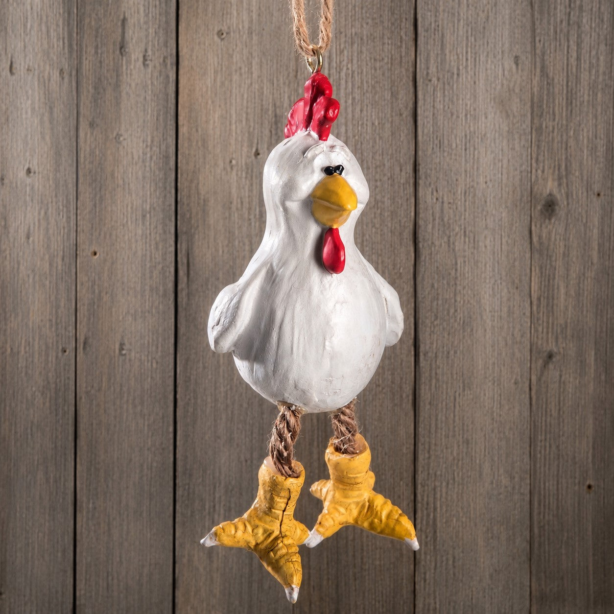 A hanging chicken ornament with a white body, red comb and wattle, yellow beak and feet, and brown rope legs, shown against a rustic wooden plank background. Cute farm animal.