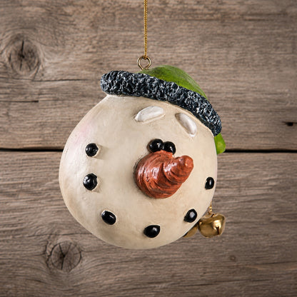 Snowman  Christmas ornament by Bert Andserson hanging against a rustic wooden plank background. 