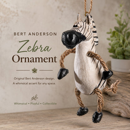Bert Anderson Zebra Ornament hanging ornament featuring a painted zebra body with black and white stripes, rope legs, and a hanging loop, shown against a rustic beige background with product text on the left.