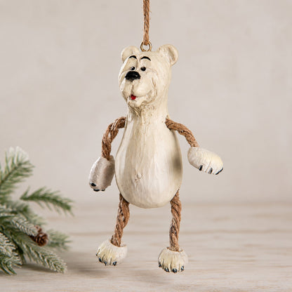 A whimsical hanging polar bear ornamnet made from resin with rope arms and legs, hanging against a neutral beige background with a pine branch in the corner.  Hanging Christmas ornament  by Bert Anderson.