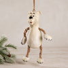 A whimsical hanging polar bear ornamnet made from resin with rope arms and legs, hanging against a neutral beige background with a pine branch in the corner.  Hanging Christmas ornament  by Bert Anderson.