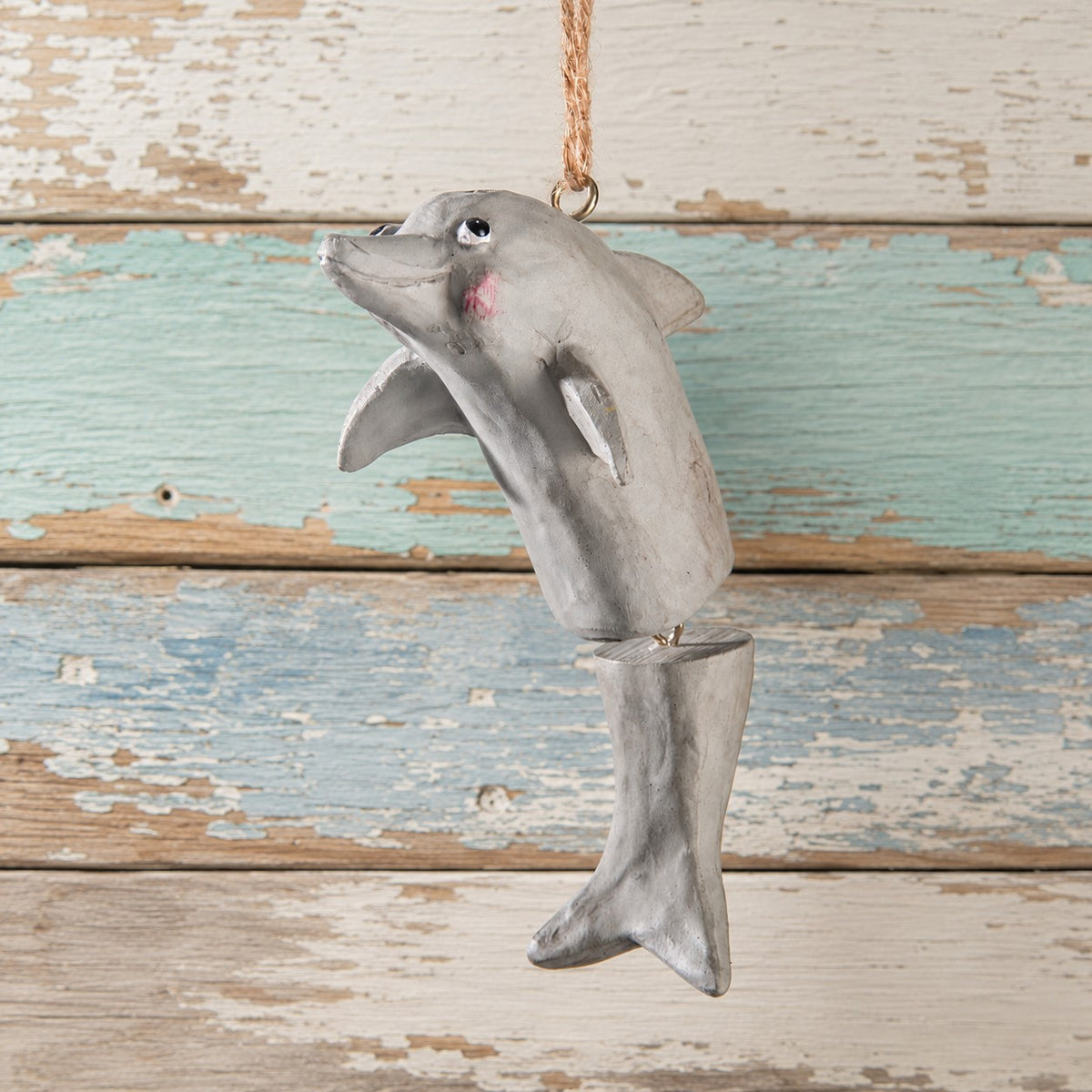 A hand painted dolphin hanging ornament with a natural twine loop at the top, shown against a distressed rustic wood plank background.