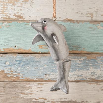 A hand painted dolphin hanging ornament with a natural twine loop at the top, shown against a distressed rustic wood plank background.