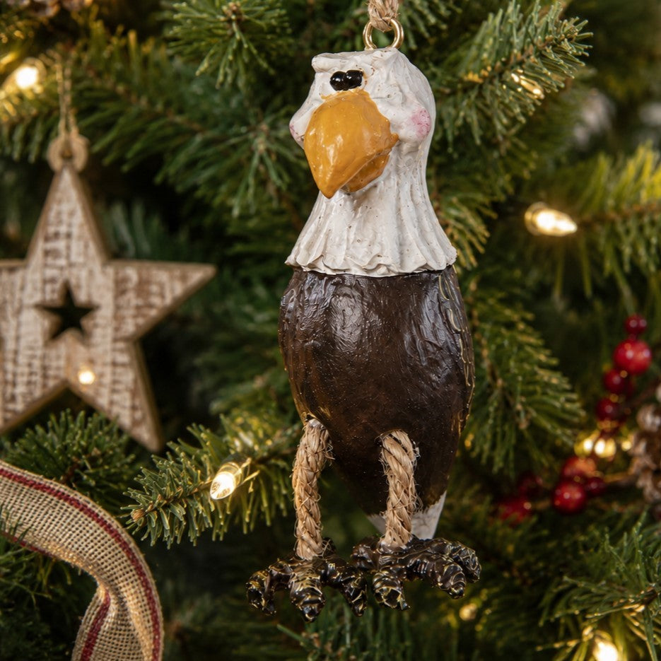 A rustic painted bald eagle Christmas ornament hanging on a decorated Christmas tree with lights and green pine branches. By Bert Anderson