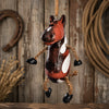 A rustic hanging horse painted in red, brown, black, and white with rope limbs and hooves, suspended against a weathered wood plank background with a horseshoe and rope props.