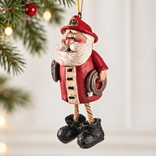 Bert Anderson firefighter Santa ornament with red fire helmet, fire hose, dangling rope legs and black boots in a bright Christmas setting.