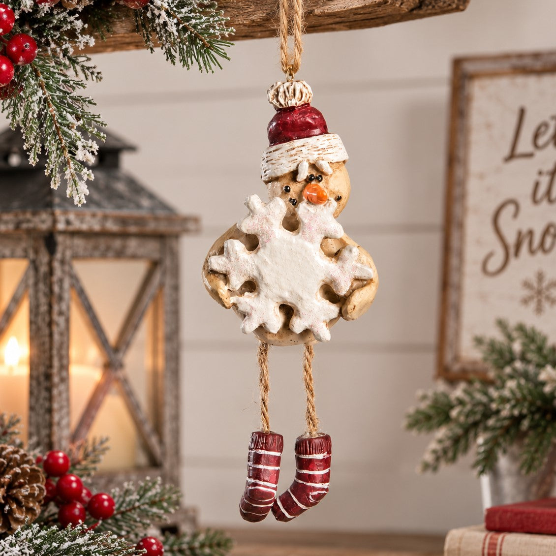 A hanging Snowman Ornament with striped leggings, red hat and carrying  a snowflake.   Winter home decor.