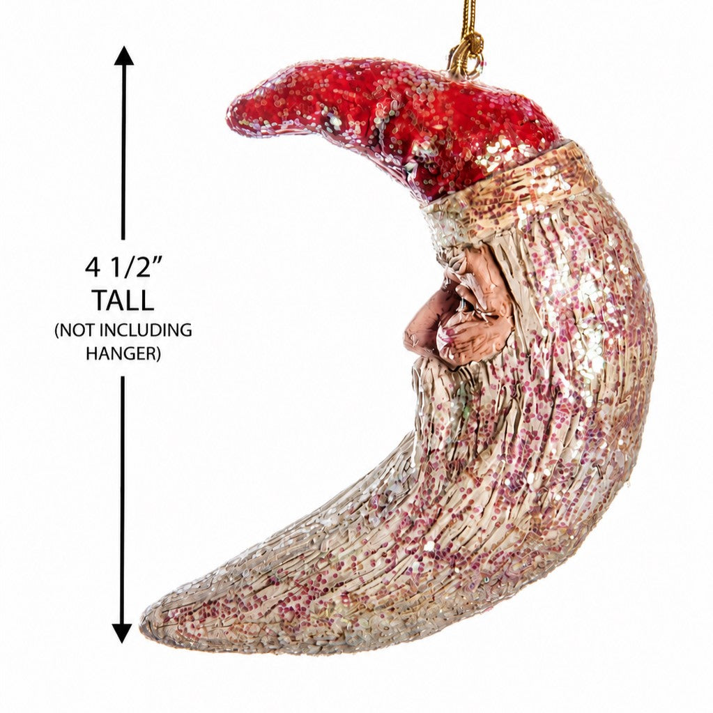 A crescent moon Christmas ornament with a red hat and a  glittery body, shown on a white background with a height measurement label of 4 1/2 inches.