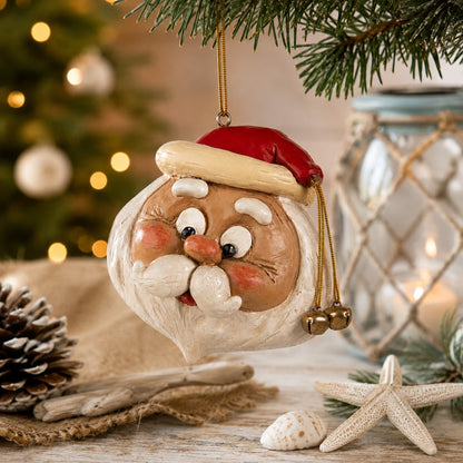 A festive Santa Claus Christmas ornament hanging from a pine branch, styled on a rustic tabletop with a blurred Christmas decor.