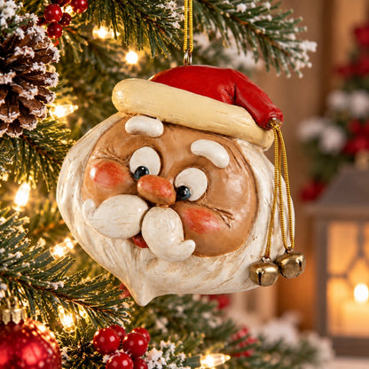 A Santa Claus head Christmas ornament hanging on a decorated Christmas tree. The ornament features gold jingle bells dangling from is red hat.  Displayed  in a holiday home decor setting.