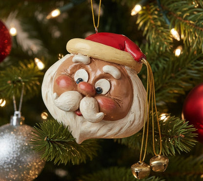 A festive Santa Claus Christmas ornament hanging on a decorated Christmas tree. The ornament features a detailed Santa face with a red hat, gold trim, white beard, and rosy cheeks, with small gold bells dangling from the side.