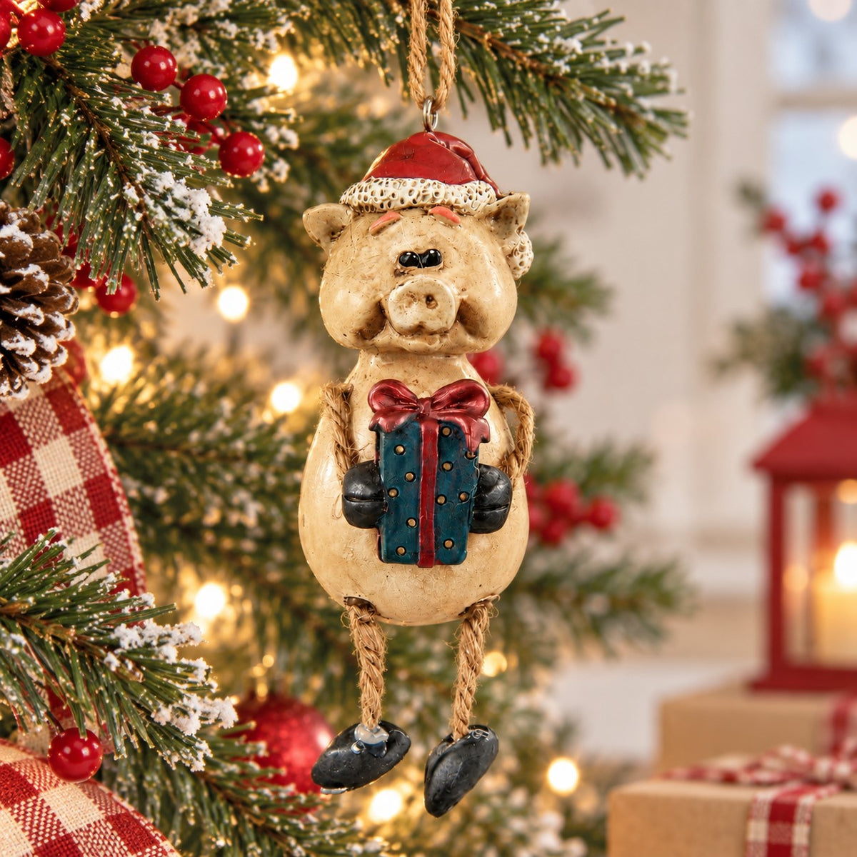 Bert Anderson pig Christmas ornament wearing a Santa hat and holding a wrapped gift, hanging among snowy evergreen branches and warm holiday lights.