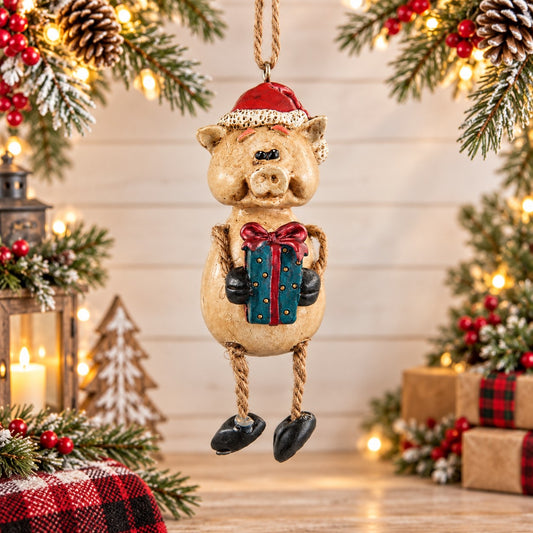 Bert Anderson pig Christmas ornament wearing a Santa hat and holding a wrapped present, displayed in a bright holiday setting with evergreen and warm lights.
