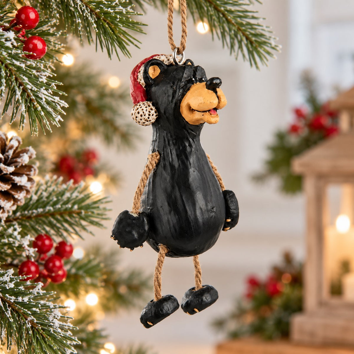 Bert Anderson black bear Christmas ornament wearing a red Santa hat with dangly rope arms and legs.