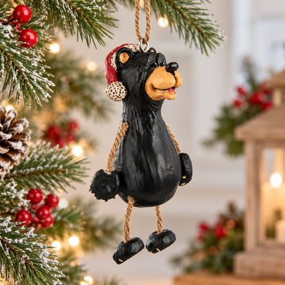 Bert Anderson black bear Christmas ornament wearing a red Santa hat with dangly rope arms and legs.