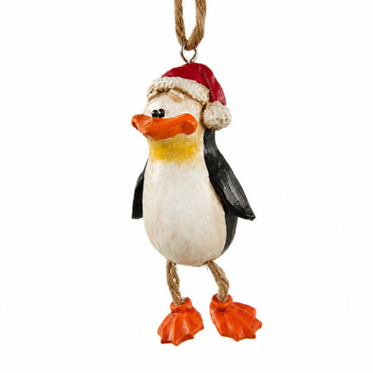 A hand painted penguin ornament wearing a red Santa hat with white trim and orange feet, hanging from a rope loop on a plain white background.