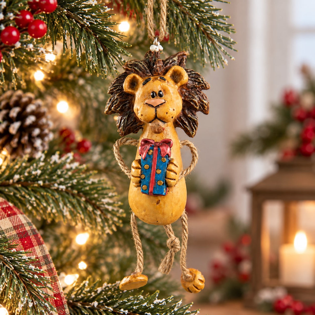 A decorative hanging lion ornament with a blue gift box with a red bow, displayed on a Christmas tree with lights and holiday decor in the background.