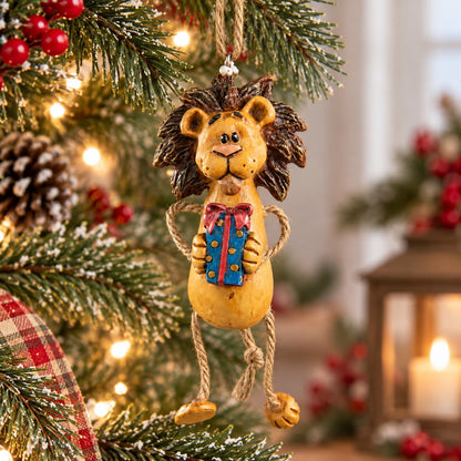 A decorative hanging lion ornament with a blue gift box with a red bow, displayed on a Christmas tree with lights and holiday decor in the background.