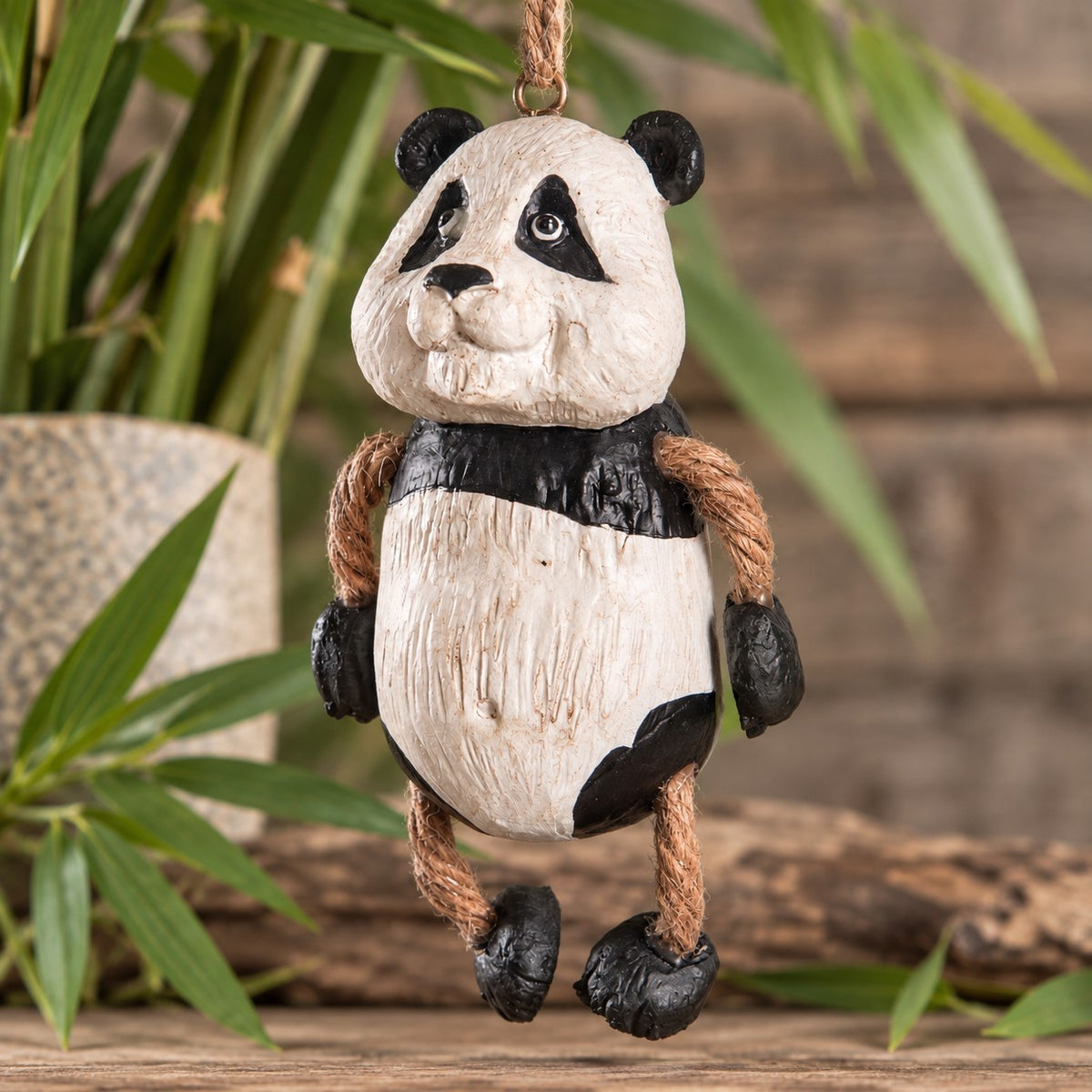Bert Anderson panda bear ornament with black-and-white coloring and dangly rope legs, hanging in a natural bamboo-inspired setting.