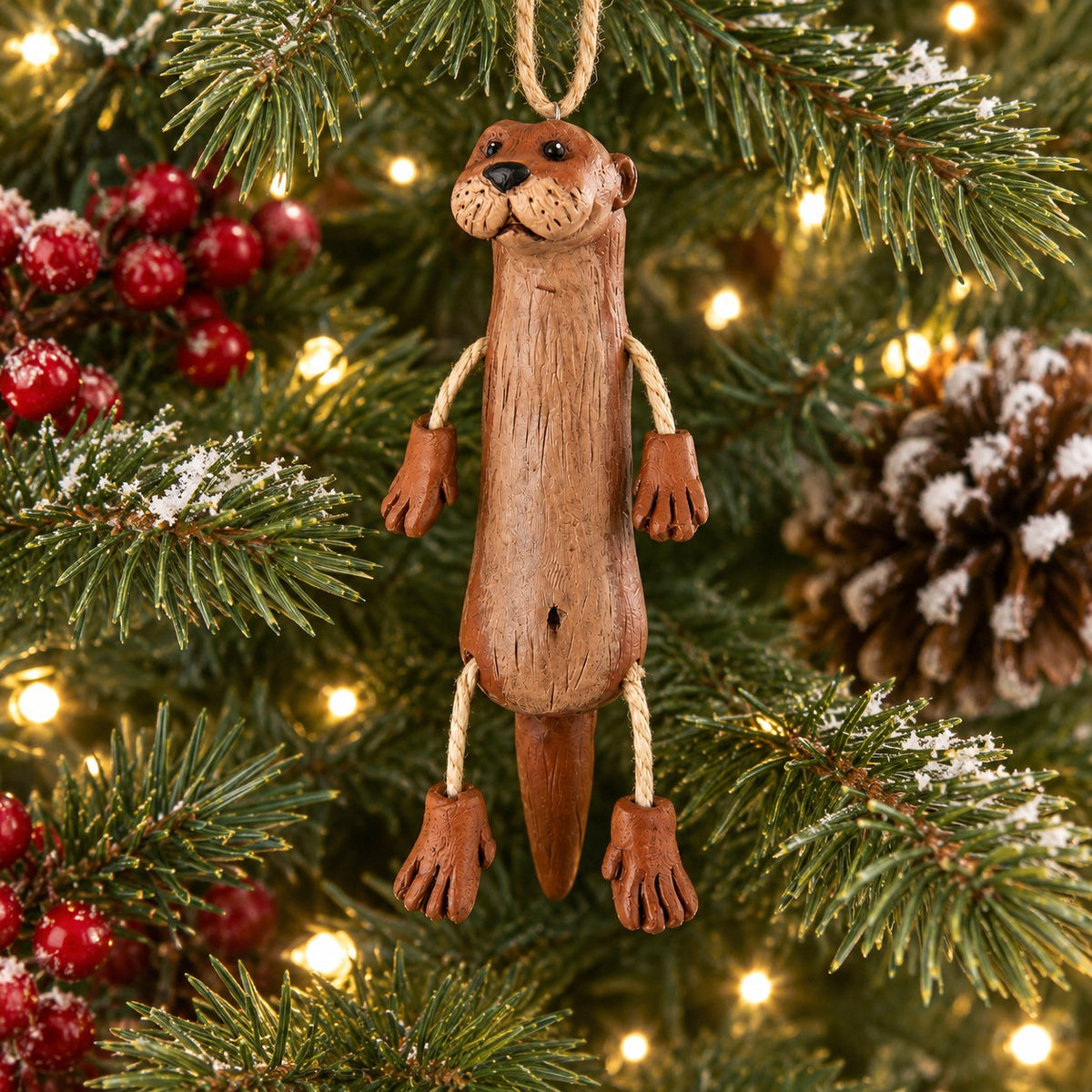 A resin otter Christmas ornament hanging from a Christmas tree.  Whimsical river otter ornament by Bert Anderson.  Woodland home decor.