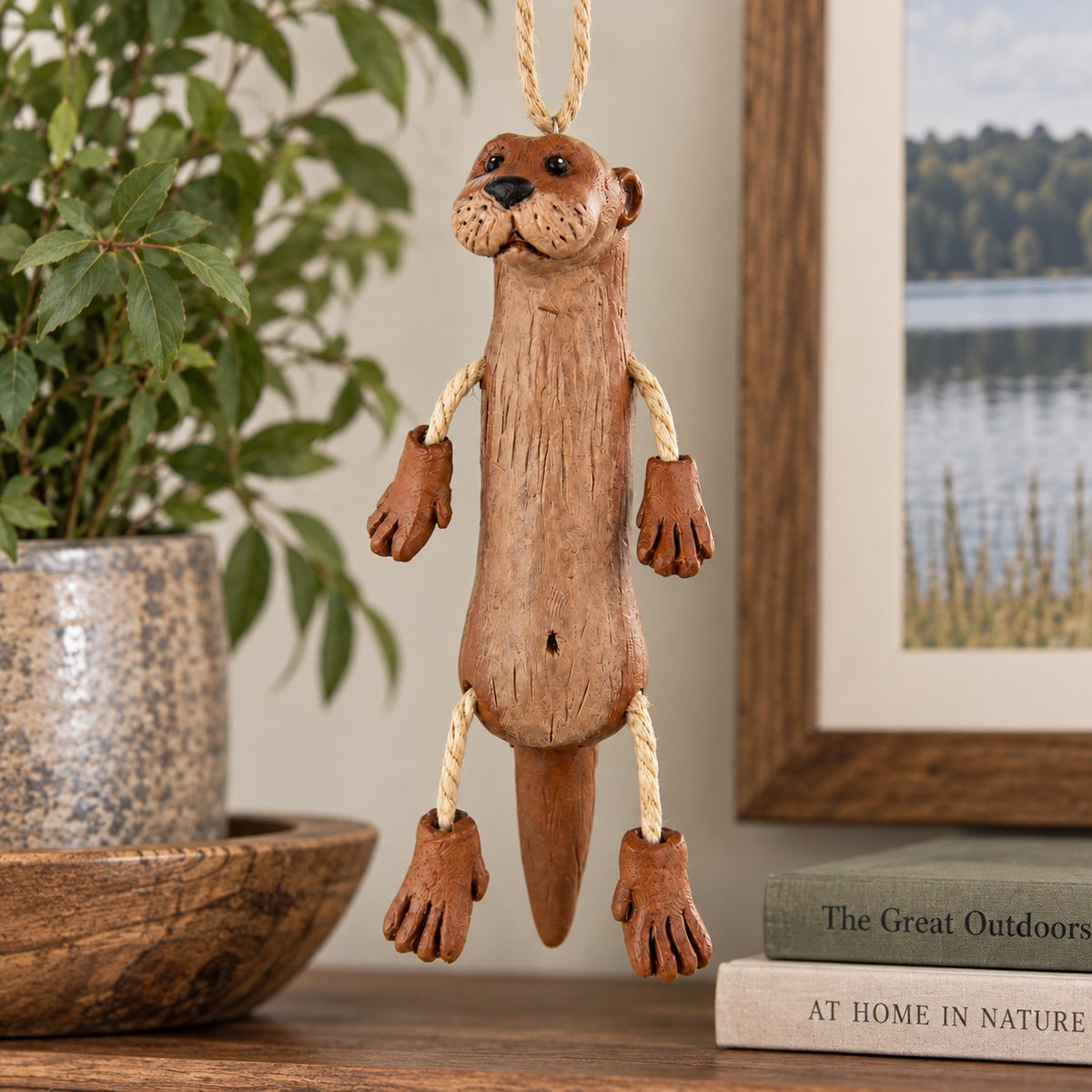 Bert Anderson river otter ornament with dangly rope arms and legs displayed in cozy lake house décor with natural wood accents and greenery.