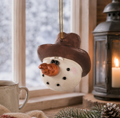 Cowboy Snowman Head Ornament from  Bert Anderson.  This snowman is wearing a brown cowboy hat an is displayed in front of winter window.