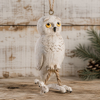 Snowy owl ornament with rope legs and big feet.  Displayed on a rustic background with Christmas pine tree branch.