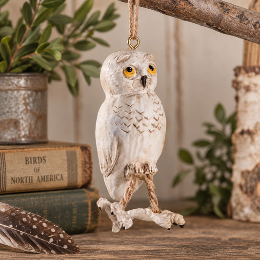 Bert Anderson snowy owl ornament with yellow eyes and dangling rope legs displayed in rustic nature-inspired décor.
