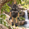 Bert Anderson gorilla ornament with dangling rope arms and legs hanging in a lush natural habitat with rocks and a waterfall.