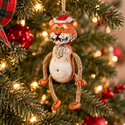 Bert Anderson tiger Christmas ornament wearing a Santa hat with dangly rope arms and legs hanging on a lighted Christmas tree.