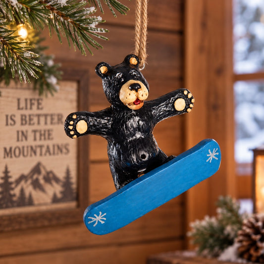 Bert Anderson snowboarding black bear ornament on a bright blue snowboard hanging in a cozy winter cabin setting.