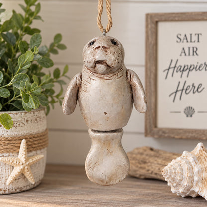 Bert Anderson manatee ornament with jointed tail hanging in a bright coastal home décor setting with seashells and greenery.