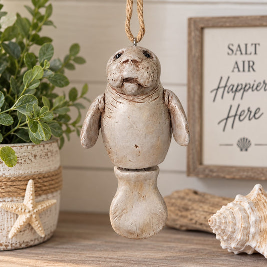 Bert Anderson manatee ornament with jointed tail hanging in a bright coastal home décor setting with seashells and greenery.