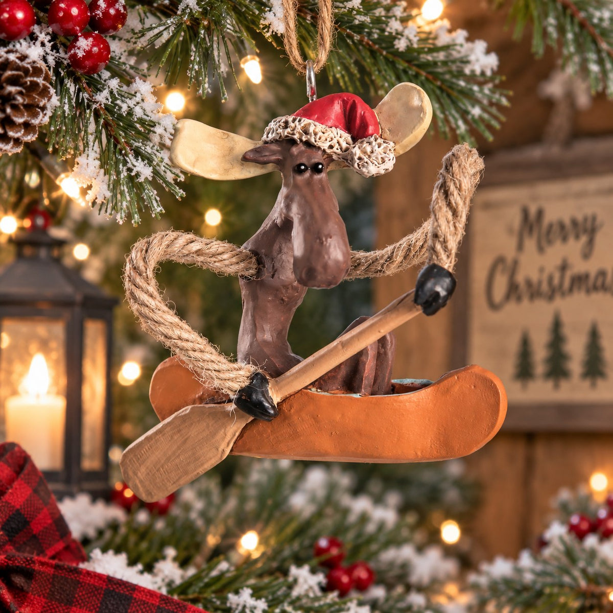Bert Anderson Christmas moose ornament wearing a Santa hat and paddling a canoe, displayed in a festive rustic holiday setting.