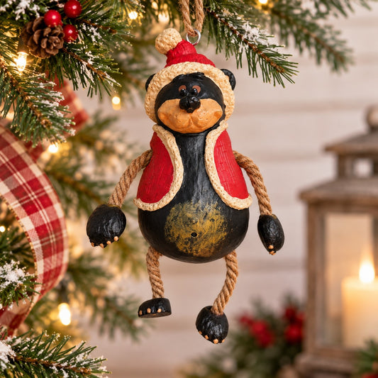 Bert Anderson Santa bear ornament wearing a red vest and Santa hat with dangly jute rope arms and legs, hanging on a Christmas tree.