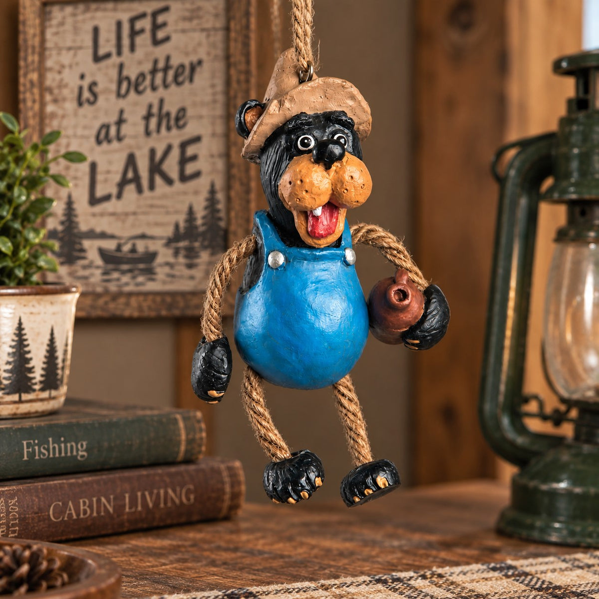 Bert Anderson Moonshine Bear ornament in blue overalls and fishing hat holding a jug, displayed in a rustic lake cabin setting.