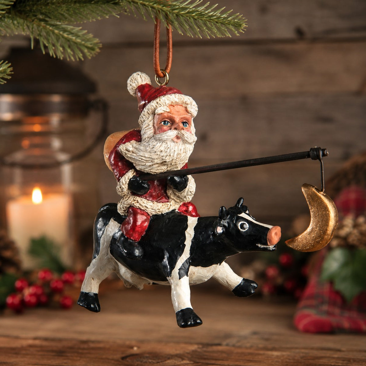 Christmas Cabin Photo: Bert Anderson Santa Riding a Cow ornament with fishing pole and dangling crescent moon, displayed in a warm rustic Christmas cabin setting.