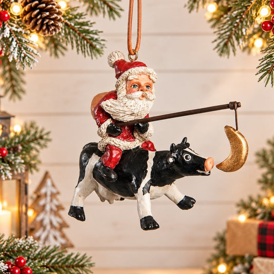 Bert Anderson Santa riding a black-and-white cow Christmas ornament, displayed against a light holiday background with evergreen, red berries and warm lights.
