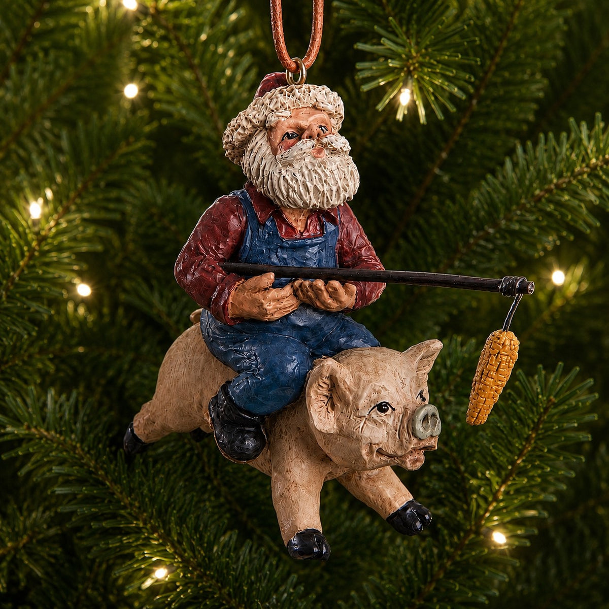 Bert Anderson Santa Riding a Flying Pig ornament with blue overalls, red shirt and Santa hat, holding a pole with dangling ear of corn on a white background.
