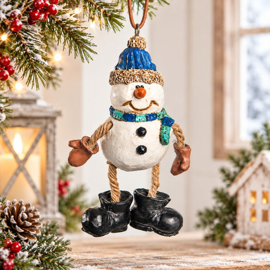 Bert Anderson snowman ornament with blue hat, scarf, rope legs and oversized black boots displayed in a bright Christmas setting.