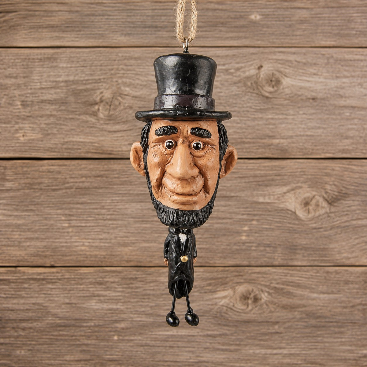 Abe Lincoln ornament with oversized head, stovepipe hat and dangling wire legs displayed against rustic barnwood.