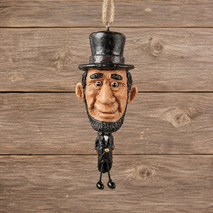 Abe Lincoln ornament with oversized head, stovepipe hat and dangling wire legs displayed against rustic barnwood.