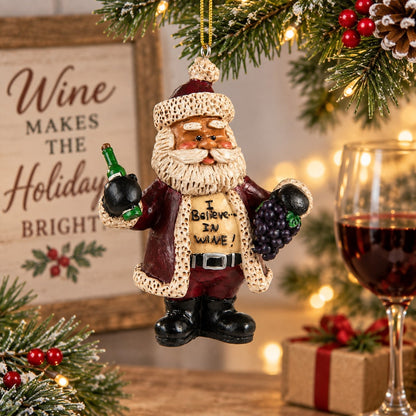 Bert Anderson “I Believe in Wine” Santa ornament holding a wine bottle and grapes in a bright Christmas setting with evergreen, lights and a glass of wine.