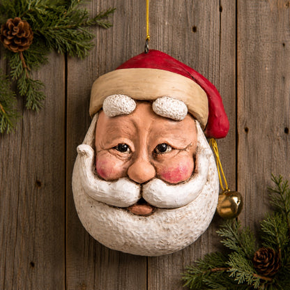 Bert Anderson large Santa face ornament with rosy cheeks, white beard and gold bells displayed against rustic wood with evergreen.