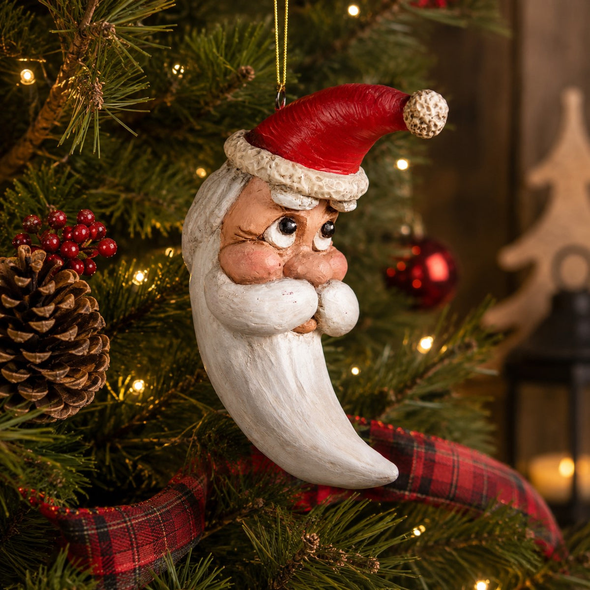 Bert Anderson crescent moon Santa ornament hanging on a Christmas tree with warm lights, pinecones and red plaid ribbon.