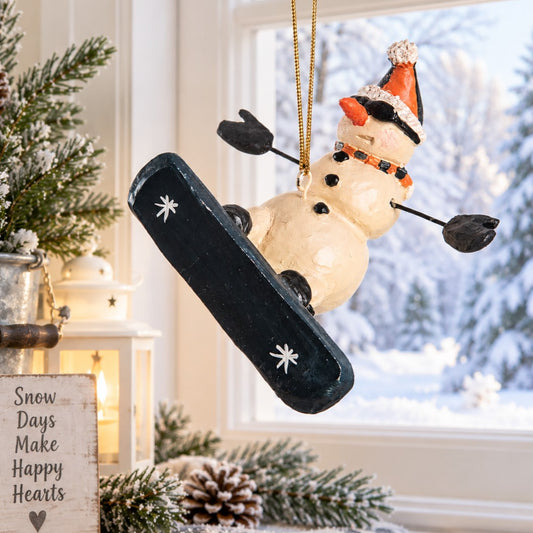Bert Anderson snowboarding snowman ornament displayed by a white-trimmed window overlooking a snowy winter scene.