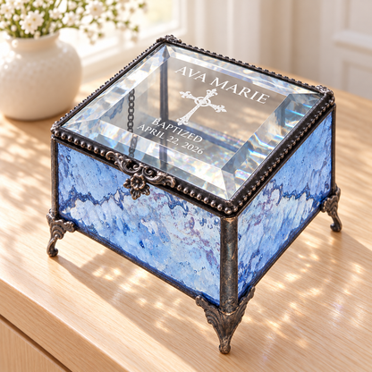 Blue textured glass baptism keepsake box engraved Ava Marie, an ornate cross, Baptized and April 22, 2026, with a clear beveled lid and decorative feet.